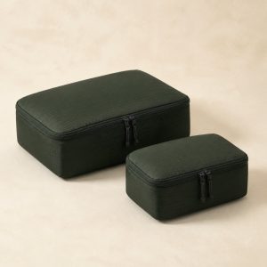 Forest-green recycled-nylon Transit Packing Cubes set on a warm ivory surface